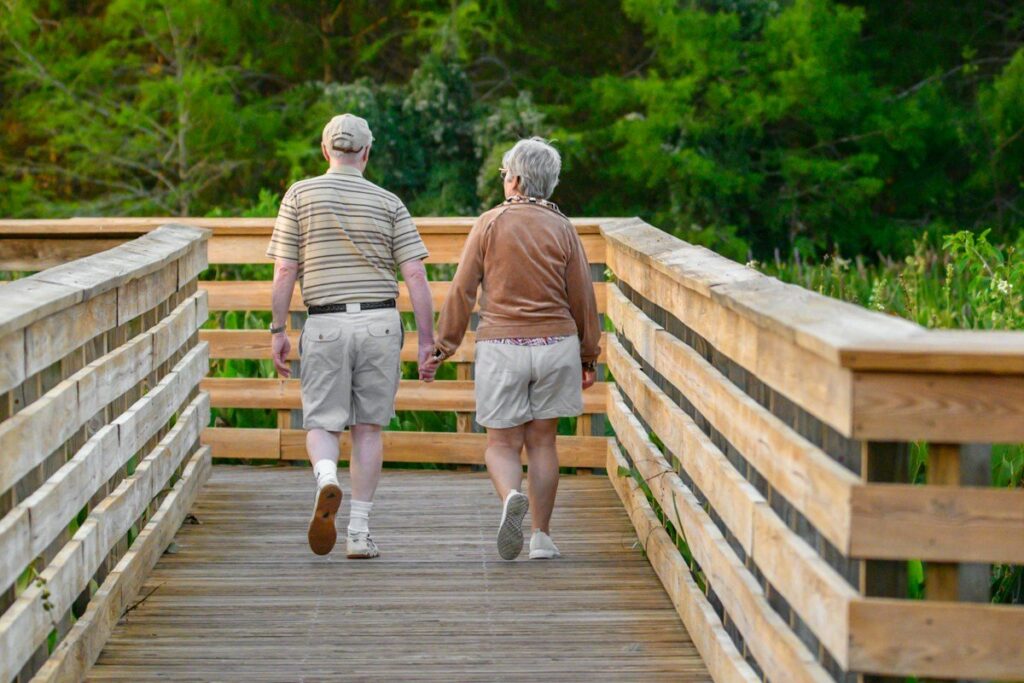 Two older adults walking together along a wooden boardwalk